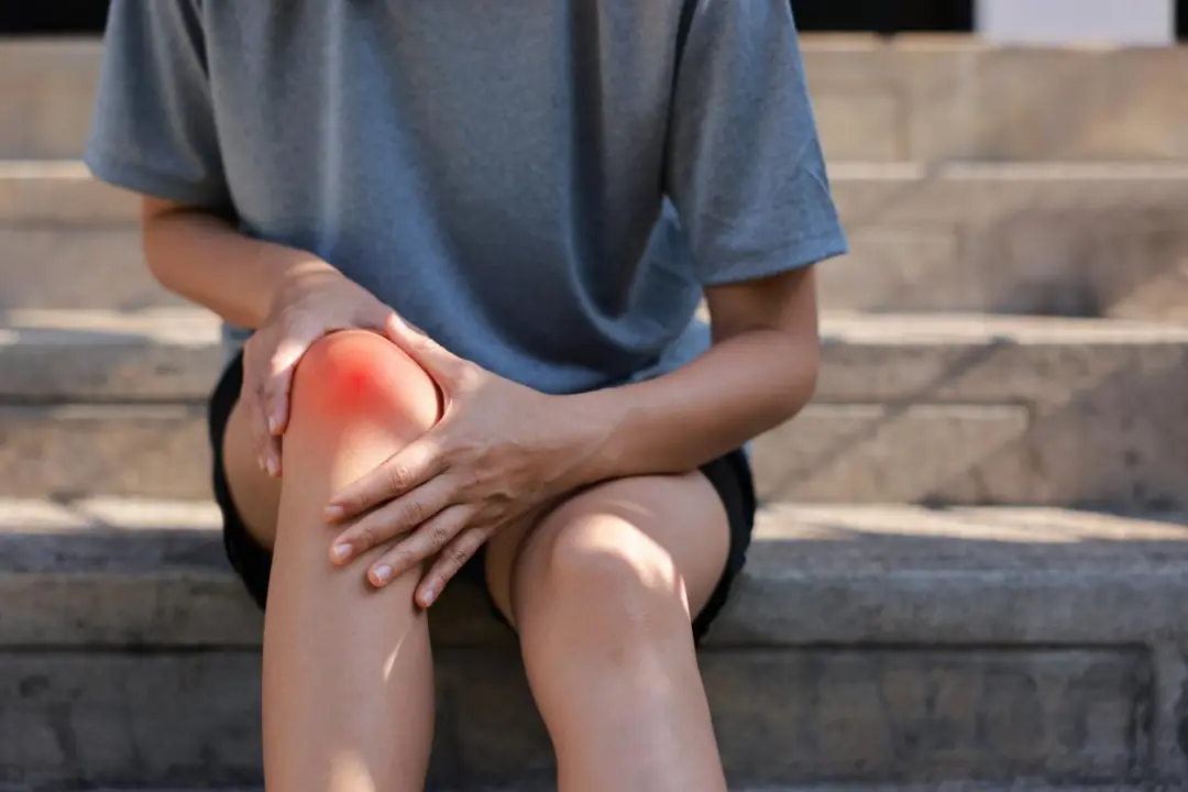 Person holding a painful knee while sitting outdoors